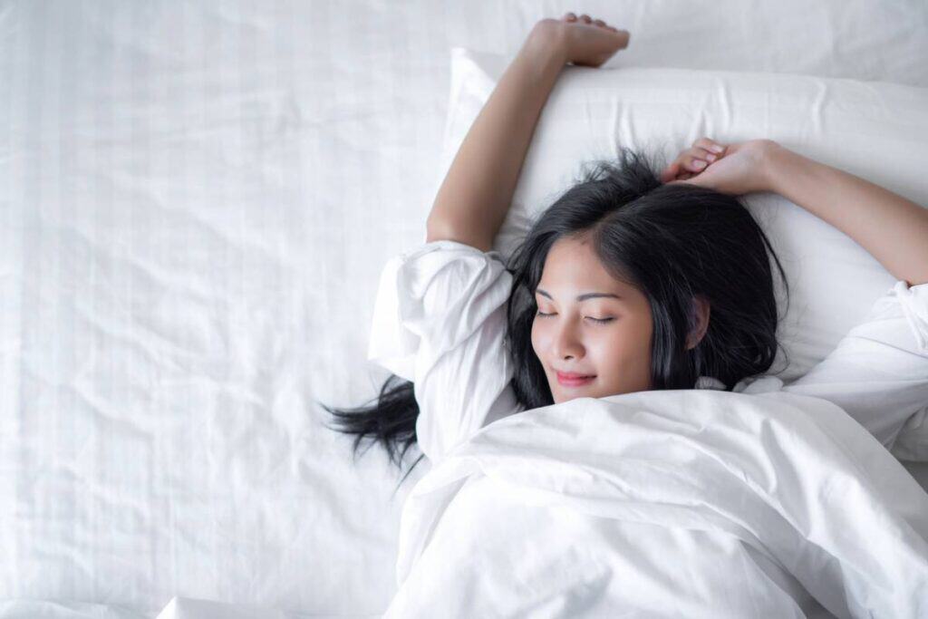 Femme souriante s'étirant dans un lit blanc.