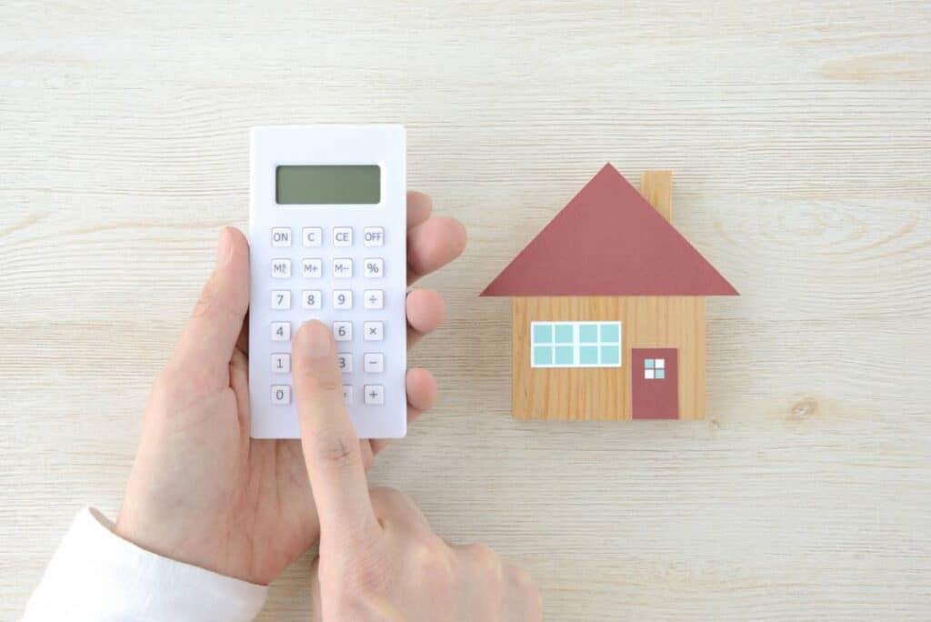 Main utilisant une calculatrice à côté d'une petite maison.