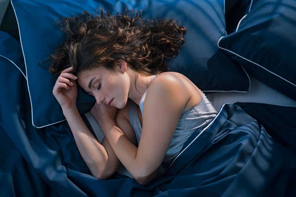 Femme aux cheveux bouclés dormant dans un lit bleu.